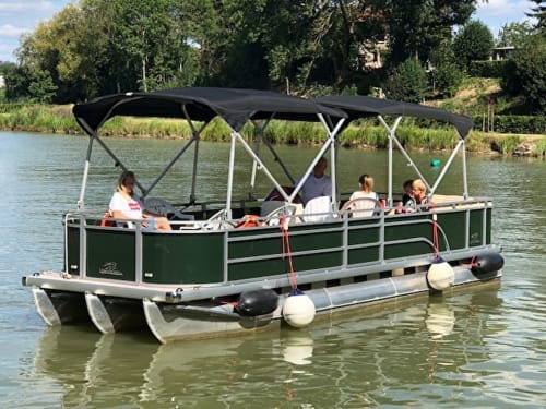 Green pontoon boat with black canopy on river near Château De Clusors, St Menoux France