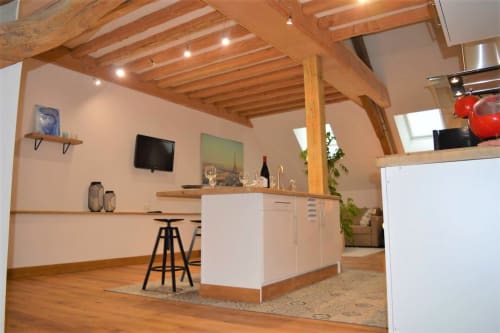 Chambre style loft moderne à la Conciergerie Des Climats à Beaune avec poutres apparentes, îlot de cuisine blanc, télévision et parquet