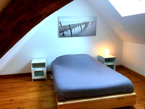 Chambre mansardée à la Conciergerie Des Climats à Beaune avec literie bleue, tables de nuit blanches, poutres en bois et vue sur l'eau