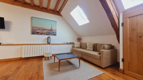 Chambre mansardée de l'hôtel Beaune avec canapé beige, table de jeu bleue, puits de lumière, œuvre parisienne, poutres en bois et radiateur