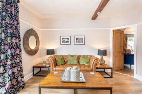 The bed and breakfast common area with large leather sofa, vibrant curtains, wooden coffee table, and character beams