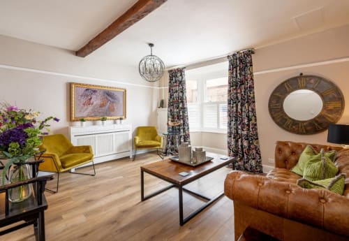 Bed and breakfast common lounge with leather sofa, wooden coffee table, mirror, acid green armchairs, vibrant curtains, and photo-framed television
