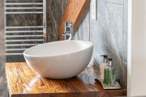 Image of one of the bathrooms; view of the bowl sink on wooden cabinet, featuring Molton Brown products