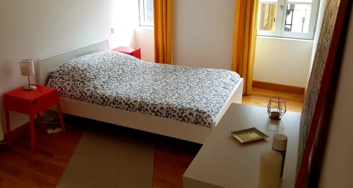 Chambre lumineuse à la Conciergerie Des Climats à Beaune avec lit blanc, table de nuit rouge, bureau et fenêtres avec vue sur la ville aux volets jaunes