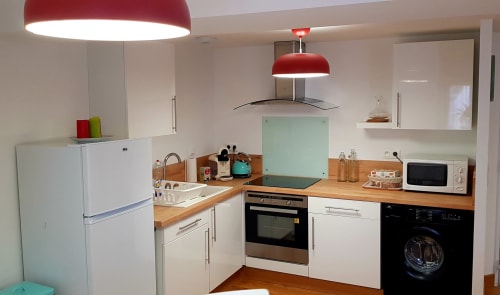 Cuisine moderne du gîte de Beaune avec armoires blanches, plans de travail en bois, suspensions rouges et électroménagers inox