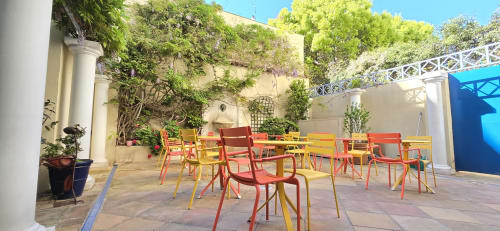 Colorful outdoor courtyard seating at Hôtel De La Fontaine in Nice with red and yellow chairs around tables under ivy-covered