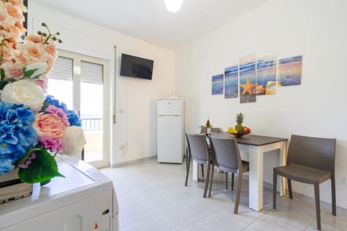 Cucina e zona pranzo moderne con vista mare, dipinti marini, tavolo da pranzo, frigorifero e decori floreali