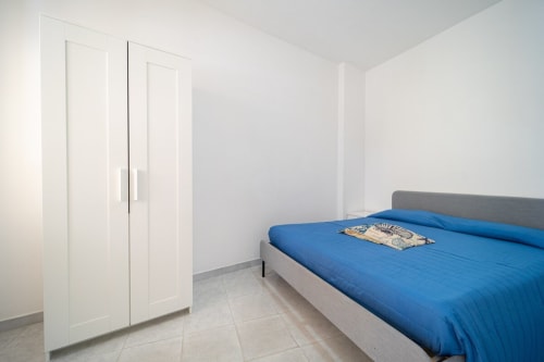 Camera luminosa con biancheria blu, guardaroba grigio e pavimento piastrellato presso l'appartamento Lux Immobiliare, Marina di Strongoli