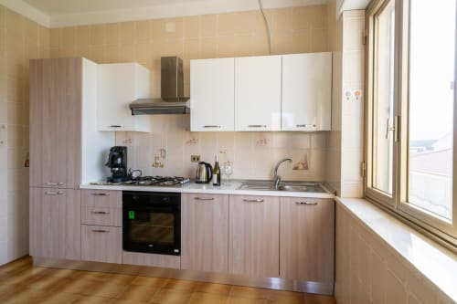 Cucina moderna con arredi bianchi e in legno, fornello a gas e finestra con vista mare nell'appartamento Lux Immobiliare a Marina di