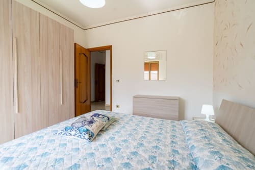 Camera luminosa con biancheria blu decorata, armadio in legno e finestra vista mare nell'appartamento fronte spiaggia di Lux Immobiliare,