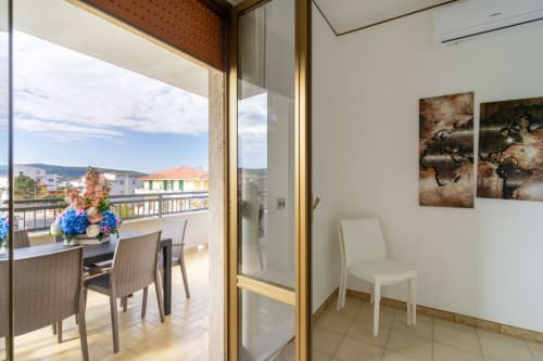 Soggiorno penthouse con balcone vista mare a Marina di Strongoli, Italia. Zona pranzo, sedie bianche e paesaggio costiero