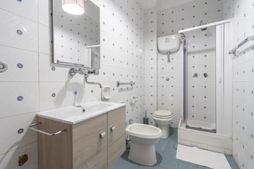 Bagno moderno con piastrelle bianche, vanità in legno, toilette, bidet e box doccia in vetro presso l'appartamento Lux Immobiliare
