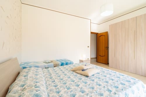 Camera da letto luminosa fronte mare con due letti singoli, piumoni blu decorati, armadio in legno e applique bianca a Lux