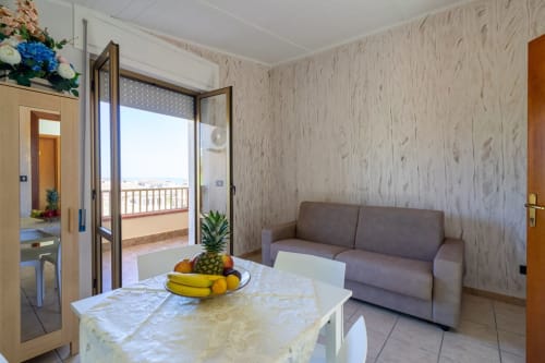 Elegante soggiorno con divano grigio, vista mare dalla terrazza e tavolo da pranzo con frutta fresca a Marina di Strongoli