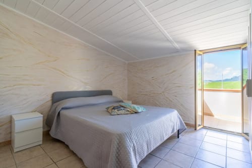 Luminosa camera da letto moderna con balcone vista mare, pareti in marmo e pavimenti in piastrelle nell'appartamento fronte spiaggia di Marina di Strongoli