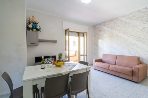 Zona pranzo di moderno appartamento con divano rosa e balcone vista mare presso Lux Immobiliare, Marina di Strongoli