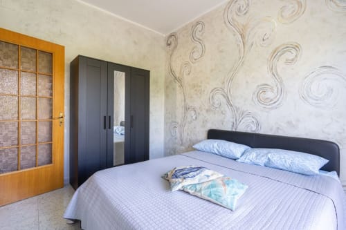 Camera moderna con letto in ferro nero, cuscini blu e carta da parati con motivo spirale decorativo presso Lux Immobiliare, Marina di Strongoli