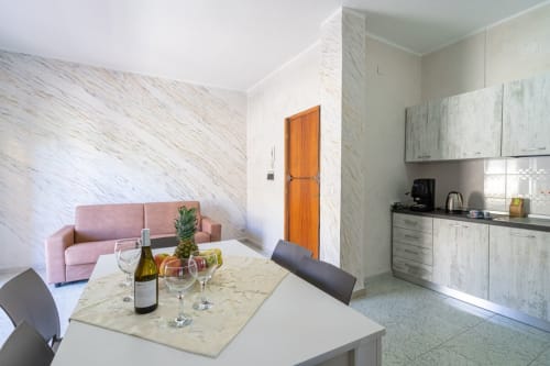 Moderno appartamento a Marina di Strongoli con divano rosa, pareti in marmo, cucina attrezzata e tavolo da pranzo preparato per il vino