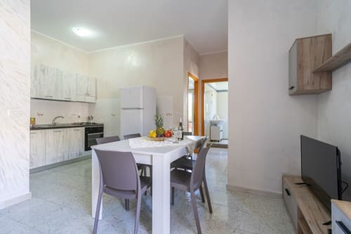 Moderna cucina-sala da pranzo con tavolo bianco, accesso al balcone con vista mare, elettrodomestici in acciaio inox a Marina di