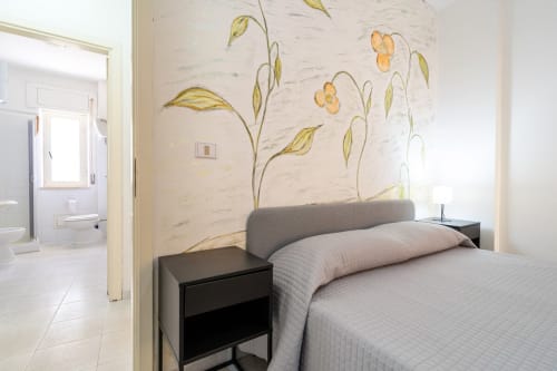 Camera da letto moderna con murale floreale, testata grigia e comodino nero in appartamento fronte mare a Marina di Strongoli
