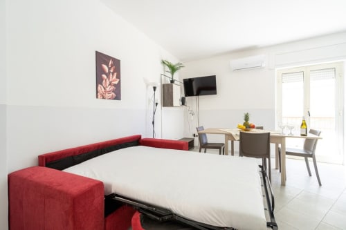 Moderno appartamento sul mare a Marina di Strongoli con divano letto rosso, zona pranzo, TV e balcone con vista mare