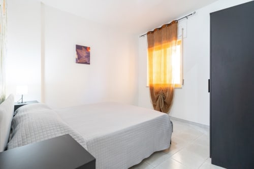 Camera luminosa con vista mare, tende dorate, letto bianco e armadio scuro nell'appartamento Marina di Strongoli