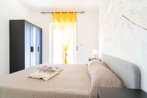 Luminosa camera con vista mare presso Lux Immobiliare B&B a Marina di Strongoli: letto matrimoniale, tende gialle e arredamento nero moderno