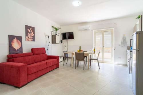Ampio appartamento vista mare a Marina di Strongoli con divano rosso, tavolo da pranzo, cucina, TV schermo piatto e accesso al balcone