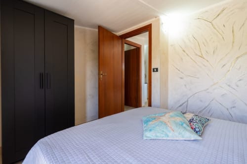 Camera da letto moderna con armadio nero, porte in legno, carta da parati con vista mare, letto matrimoniale con cuscini decorativi a Lux Immobiliare,