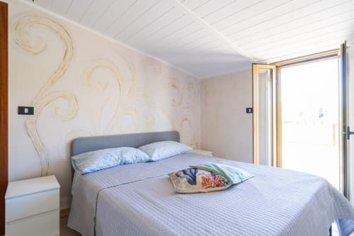 Camera luminosa con vista sul mare a Lux Immobiliare, Marina di Strongoli. Cuscini blu, decorazioni murali, accesso alla terrazza.