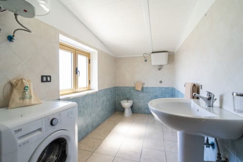 Bagno moderno nell'appartamento Lux Immobiliare di Marina di Strongoli, con lavatrice, lavabo a colonna, bidet e piastrelle blu