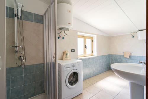 Bagno moderno Lux Immobiliare con doccia walk-in, vasca, lavatrice, lavabo su colonna e dettagli in piastrelle blu.