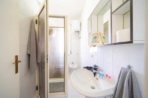 Bagno luminoso nell'appartamento di Marina di Strongoli con piastrelle bianche, lavandino, specchio, doccia e vista mare presso Lux