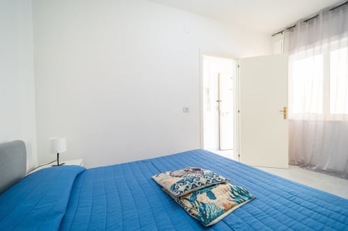 Camera luminosa con letto blu trapuntato, cuscini decorati e porte con vista mare a Lux Immobiliare Marina di Strongoli