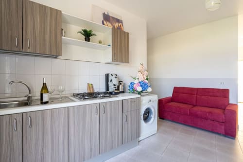 Cucina moderna con fornello a gas, lavatrice bianca e divano rosso nell'appartamento di Marina di Strongoli
