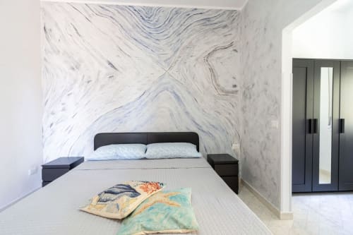 Camera da letto moderna con parete in marmo, letto con struttura nera e cuscini colorati nell'appartamento fronte mare di Lux Immobiliare