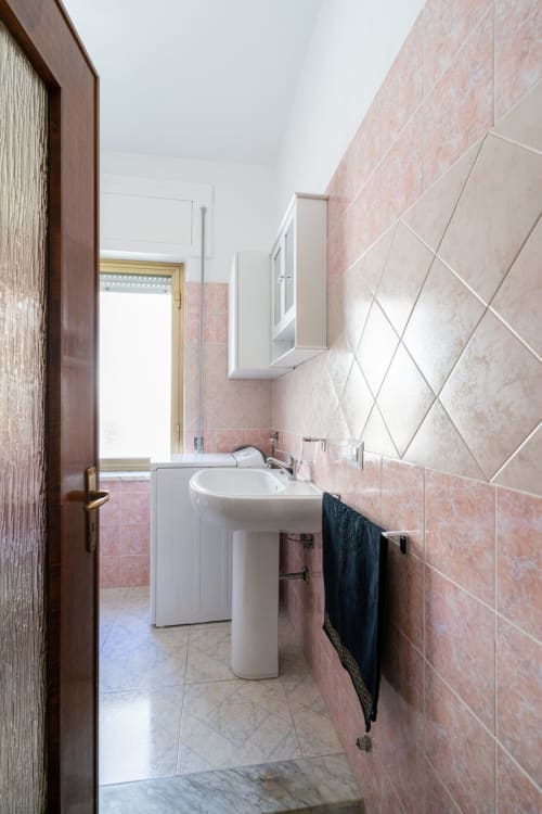 Bagno moderno con piastrelle rosa, lavabo bianco su piedistallo e porta asciugamani nell'appartamento fronte mare di Marina di Strongoli