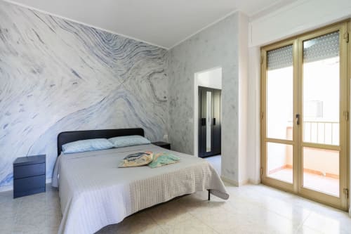Camera da letto moderna con parete in marmo, accesso al balcone con vista sul mare e arredi contemporanei a Casa a due passi dal mare