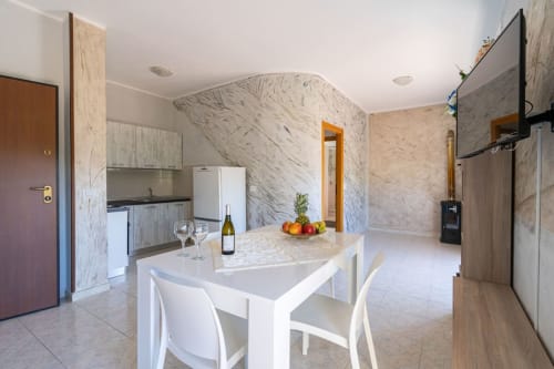 Cucina e zona pranzo di moderno appartamento con isola in marmo, sedie bianche e elettrodomestici in acciaio inox a Marina di