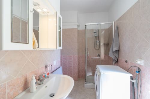 Bagno moderno con piastrelle rosa, lavabo, box doccia e lavatrice a Casa a due passi dal mare, Marina di