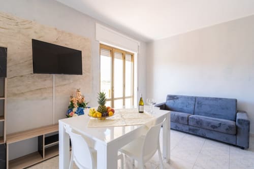 Zona giorno moderna con TV schermo piatto, tavolo da pranzo, divano blu e porte con vista mare - Casa a due passi dal mare