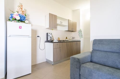 Cucina e soggiorno vista mare con frigorifero bianco, mobili in legno, divano grigio e fiori colorati