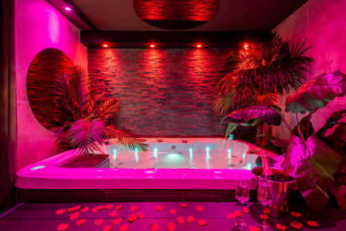Spa luxueux avec bain à remous L'Insolite, éclairage rose néon et rouge, plantes tropicales et bougies parfumées à Toulouse