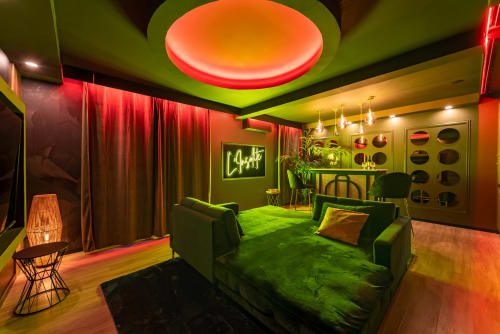Lounge moderne du L'Insolite Spa Privatif à Toulouse avec néons, plafond vert, rideaux rouges et sièges confortables