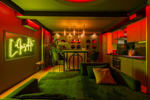 Lounge néon vibrant du spa-hôtel L'Insolite à Toulouse avec sièges verts, murs rouges et cuisine moderne