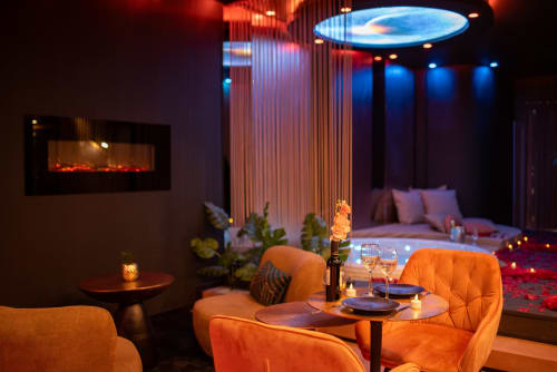 Appartement spa luxueux à L'Insolite à Toulouse avec sièges oranges, coin repas, cheminée et éclairages néon bleus au plafond