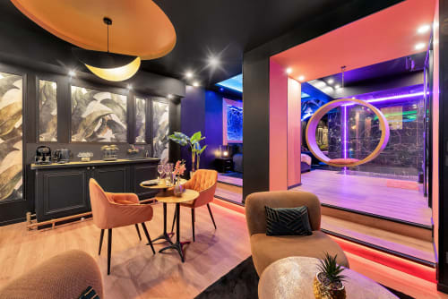 Lounge moderne à l'hôtel spa L'Insolite à Toulouse avec cloison vitrée néon, chaises orange, minibar et ambiance vibrante