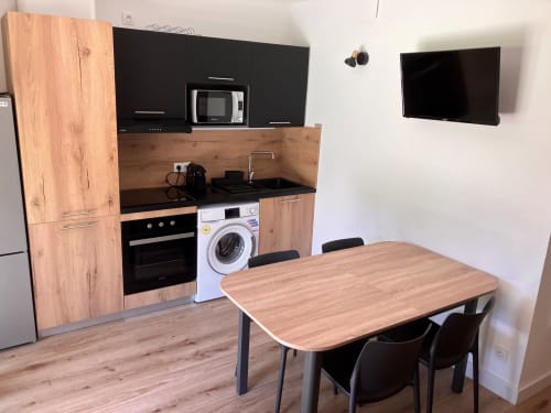 Modern kitchen and dining area in ALMA ROSSA villa, Lecci with wooden cabinetry, dining table, and wall-mounted TV