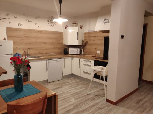 Cuisine-salle à manger moderne dans l'appartement Location MarjoRI avec placards blancs, dosseret en bois et vue sur les montagnes au
