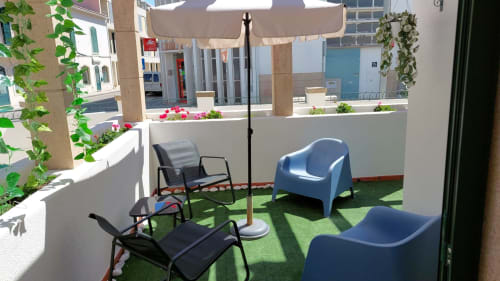 Terraço ensolarado da Villa Sor em Ponte de Sor com cadeiras azuis, espreguiçadeiras pretas, guarda-sol, grama artificial e jardineiras brancas